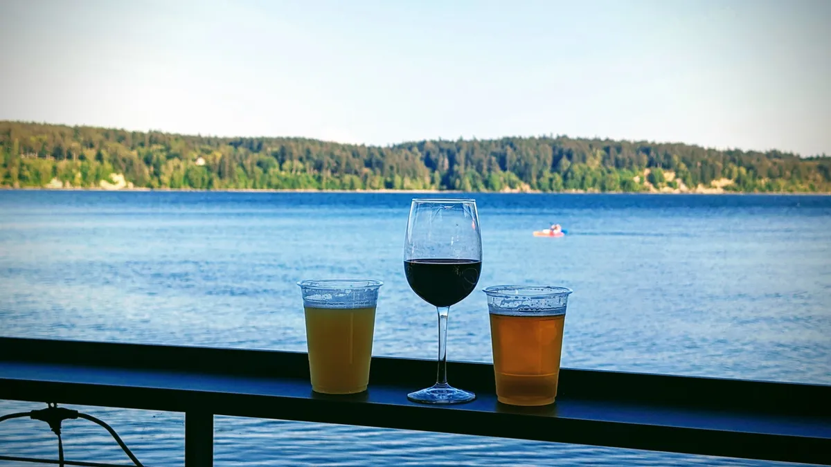 Two beers and a glass of red wine lined up on the patio rail, a kayaker out on the bay behind them