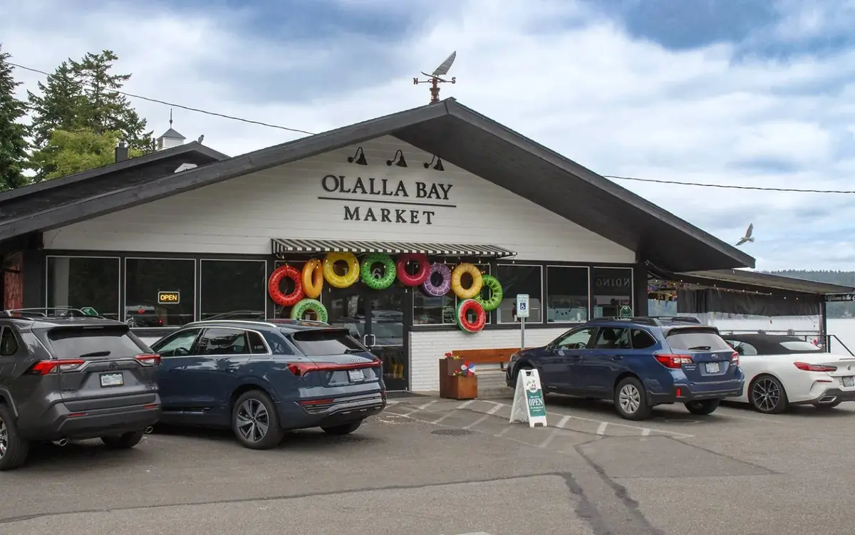 The Olalla Bay Market storefront by day, bright pool floats hung around the door and the bay behind