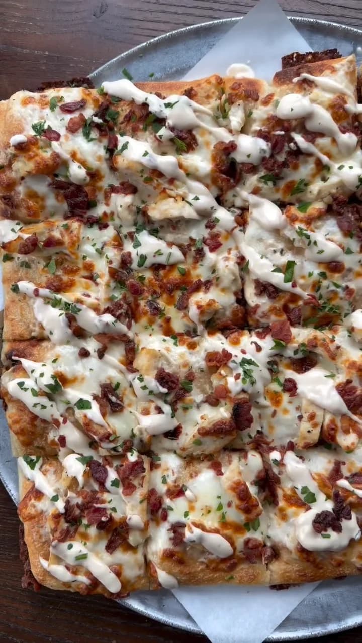 Overhead view of this week's square sourdough pizza: chicken, crispy bacon, an Alfredo drizzle and chopped parsley
